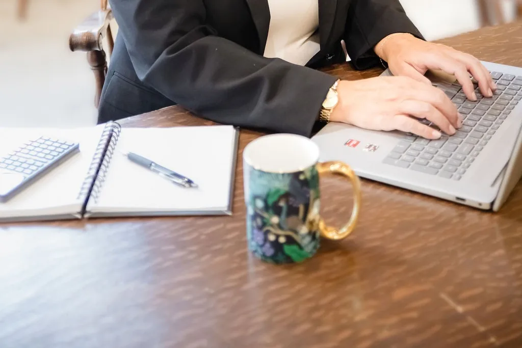 Natalia’s hands on her laptop keyboard beside a notebook, a calculator and her coffee mug