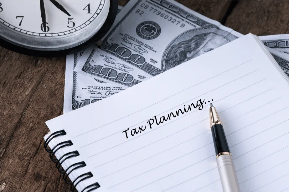 A notebook open to a page headed “Tax Planning”, with a pen, a clock and cash beside it